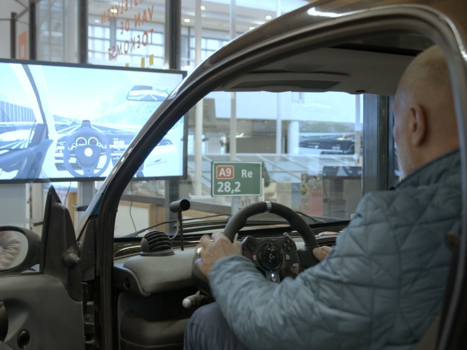 A man in the driving simulator. In front of him is a screen showing the image he sees.