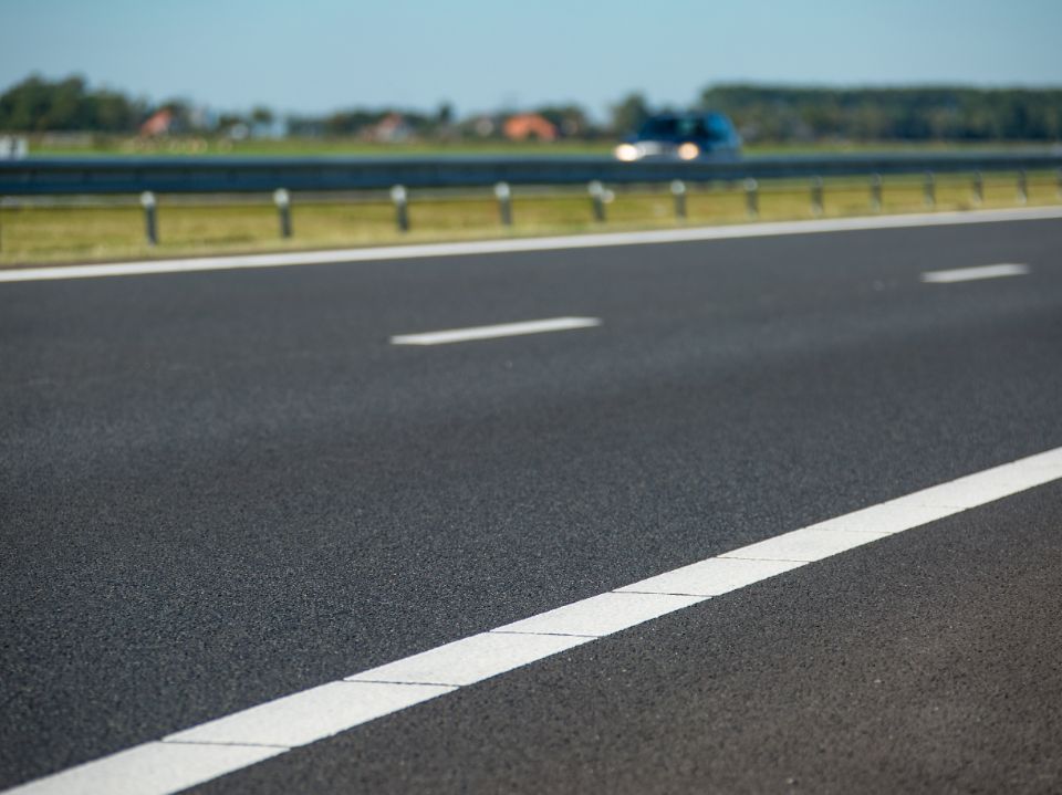 Een foto van het asfalt met witte lijnen van een snelweg.