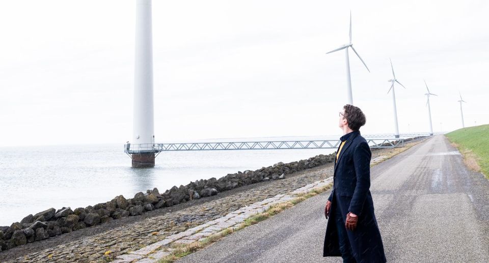 Jimme Zoete kijkt omhoog naar een windmolen. Ook in de achtergrond staan meerdere windmolens.