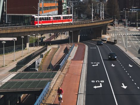 Foto van een weg met auto's, een fietspad en een trein op de achtergrond.