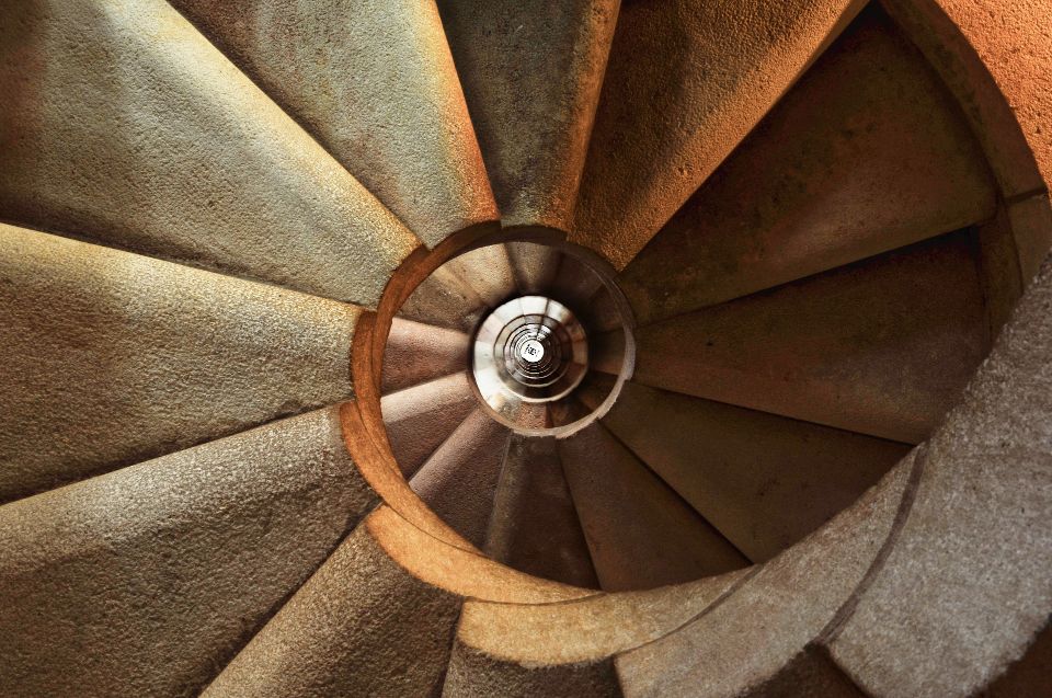 Een foto van een ronde trap, gemaakt van boven. De trap heeft een bruine kleur.